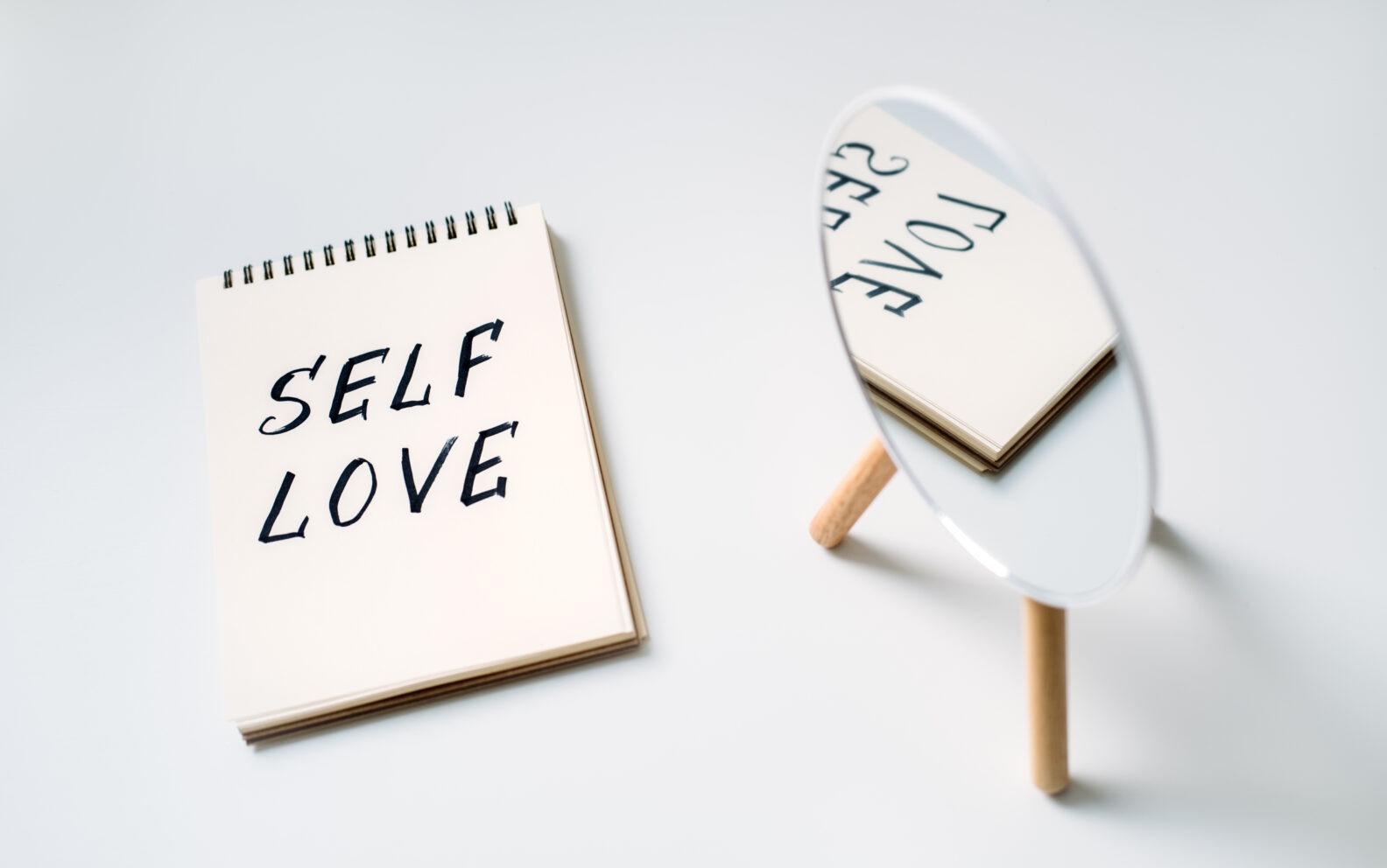 Self love, state of appreciation for oneself, physical, psychological and spiritual growth, taking care of own needs, wellbeing. Notepad with text Self love and reflection in the mirror